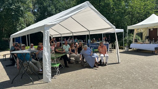 Mehrere Menschen sitzen unter einem großen, offenen Zelt