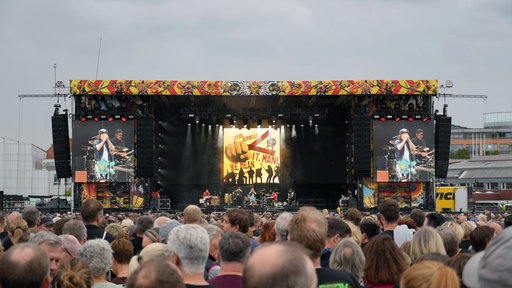 Das Publikum steht vor einer Konzertbühne auf der eine Band spielt.