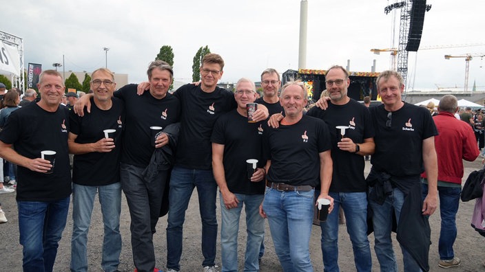 Neun Männer in schwarzen T-Shirts lächeln in die Kamera.
