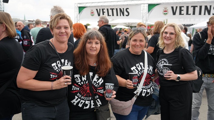 Eine vierköpfige Frauengruppe in Toten-Hosen-Fan-Shirts lächelt in die Kamera.