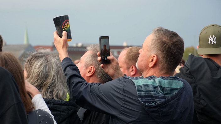 Ein Fan macht bei dem Toten Hosen Konzert in Münster ein Erinnerungsfoto von seinem Getränkebecher.