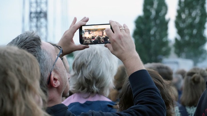 Ein Fan macht ein Video von dem Konzert auf dem Handy.
