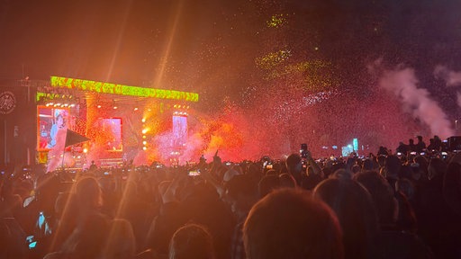 Die Konzert-Bühne bei Dunkelheit mit roten Lichtern und Fans davor.