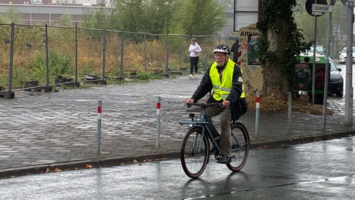 Ein Mann mit Warnweste und Helm auf einem Fahrrad
