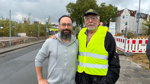 Zwei Männer mit Brille. Einer trägt eine Warnweste.