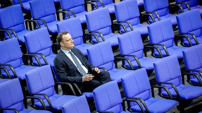 Jens Spahn sitzt alleine zwischen den blauen Stühlen im Bundestag.