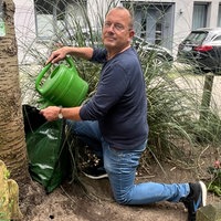 ein Mann füllt einen Beutel mit Wasser an einem Baum in einem Blumenbeet