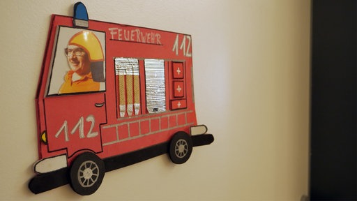 An der Wand hängt ein gebasteltes Feuerwehrauto mit Jürgen Deerhake als Fahrer