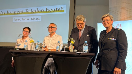Vier Personen stehen nebeneinander auf der Bühne und lächeln in die Kamera.