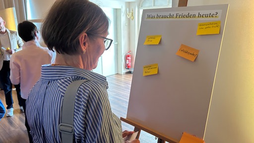 Eine Zuschauerin steht vor einer Mitmach-Tafel. An dieser sind bunte Zettel angebracht.