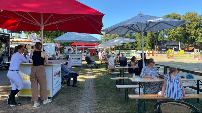 Das Publikum sitzt am Rand unter Sonnenschirmen.