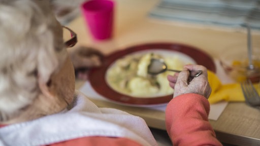 Eine Seniorin sitzt allein am Tisch und isst.