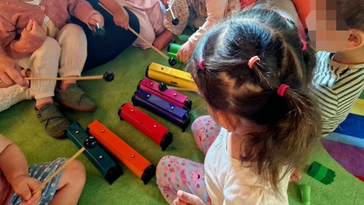 Kleinkinder spielen mit bunten Xylophon-Elementen.