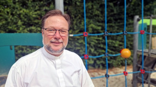 Jochen Kosmann lächelt vor einem Klettergerüst in die Kamera.