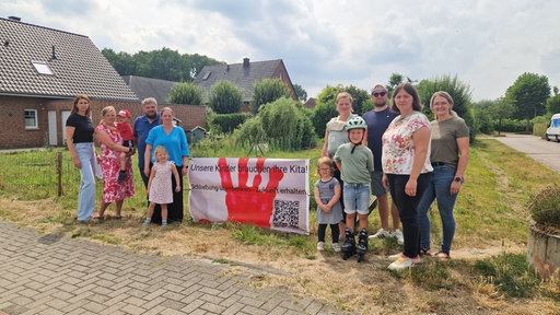 Eltern und Kinder stehen neben einem Schild: "Unsere Kinder brauchen ihre Kita!"