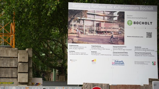 Auf dem großen Bauschild neben einem Kran stehen Infos zur Sanierung von Rathaus und Kulturzentrum