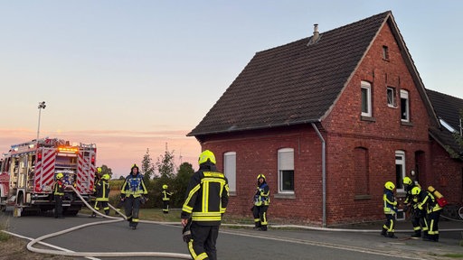 Feuerwehrleute mit Löschfahrzeug vor einem kleinen Haus.
