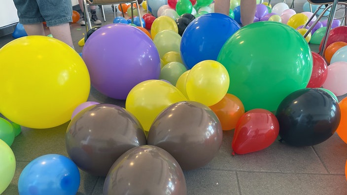 Bunte Luftballons auf dem Boden zwischen Stühlen.