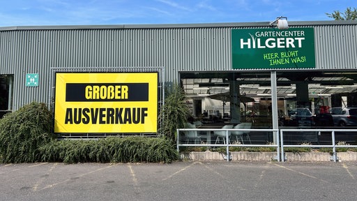 Foto vor dem Gartencenter Hilgert mit einem großen gelben Plakat mit der Aufschrift "Großer Ausverkauf".