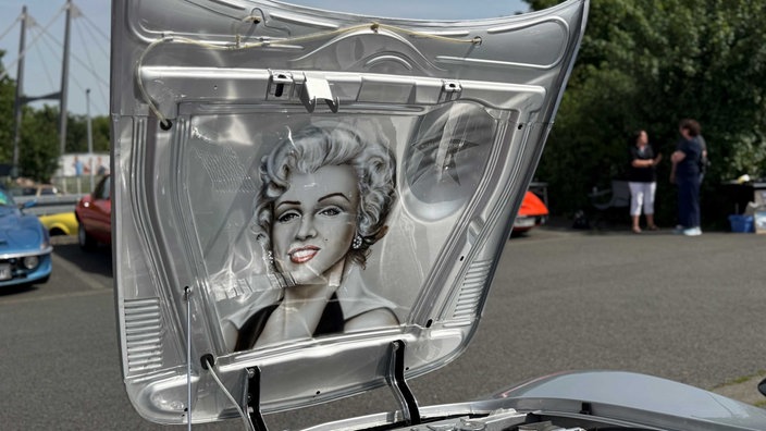 Eine aufgeklappte Motorhaube eines Opel GTs. Auf ihr ist das Bild von Mirilyn Monroe.