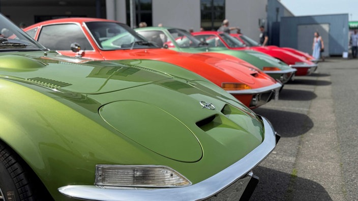 Zwei grüne Opel GTs, ein roter und einer in orange stehen in einer Reihe.