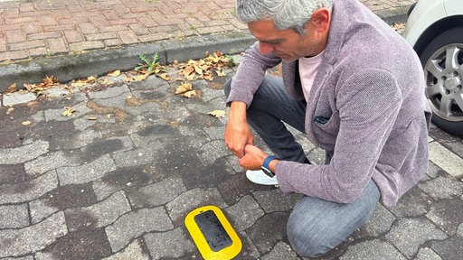Digitalbeauftragte der Stadt Bocholt Hany Omar kniet vor einem der intelligenten Parksensoren.