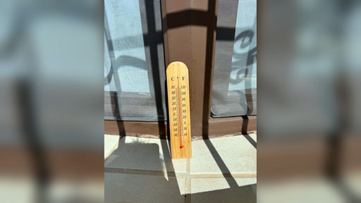 Ein kleines Thermometer lehnt an einem Fenster