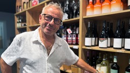 Ein Mann mit Brille steht vor einem Weinregal.