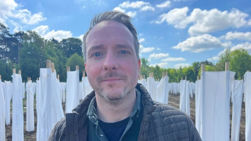 Boris Kampshoff steht auf einem Feld in Raesfeld, im Hintergrund stehen junge Bäume, eingepackt in weiße Baumwollhüllen