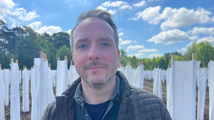 Boris Kampshoff steht auf einem Feld in Raesfeld, im Hintergrund stehen junge Bäume, eingepackt in weiße Baumwollhüllen