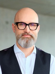 Ein Mann mit Brille und Vollbart schaut in die Kamera.