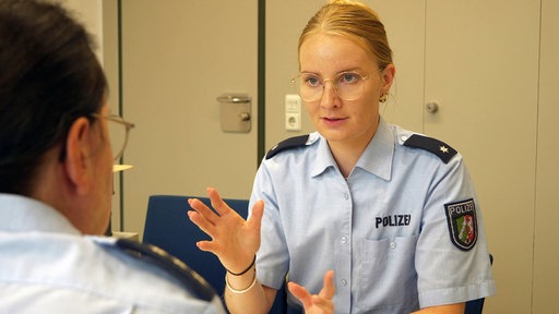 Polizistin Julia Hoffboll im Gespräch mit einem Kollegen der mit dem Rücken zu uns sitzt.