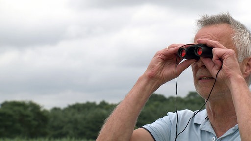 Martin Frenk, Vorsitzender NABU-Kreisverband Borken, schaut durch ein Fernglas und beobachtet Störche.