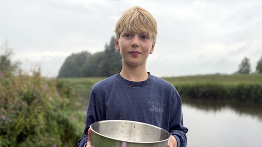 Ein Junge hält einen Eimer in die Kamera.