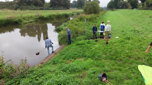 Eine Gruppe Menschen nimmt Wasserproben am Fluss.