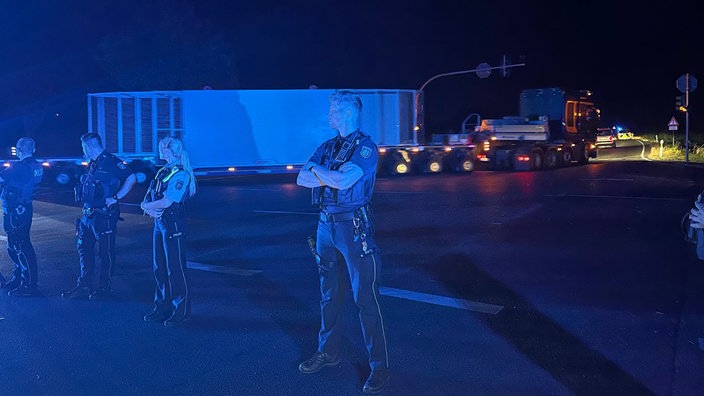 Ein Polizist schützt einen Castor-Transport, der im Hintergrund über eine Kreuzung fährt.