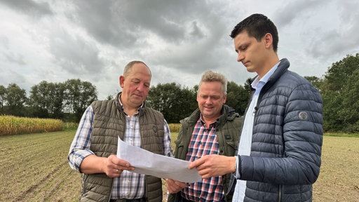 Die Landwirte Bernhard Borgert, Thomas Wesbuer und Lukas Wolters begutachten eine Karte auf dem Feld.