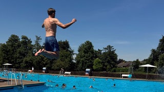 Ein Junge springt vom Einer ins Freibad.