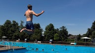 Ein Junge springt vom Einer ins Freibad.
