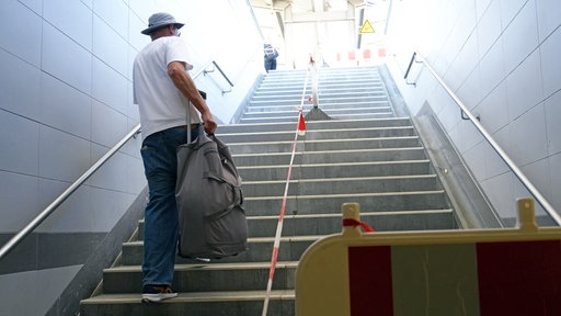Ein Mann mit Koffer läuft neben einer Baustelle die Treppe hoch.