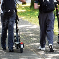 Zwei Menschen schieben jeweils einen E-Scooter neben sich her.