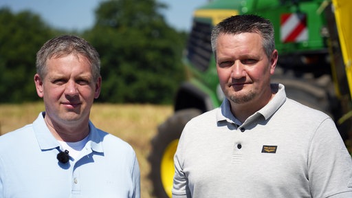 Zwei Männer stehen auf einem Feld mit einem Traktor im Hintergrund
