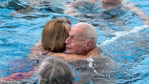 Der 100-Jährige Willi umarmt eine Frau im Wasser