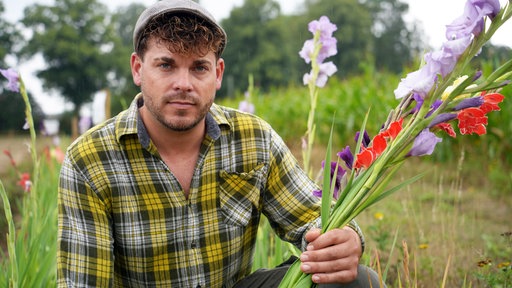 Ein Mann mit lockigen Haaren und einer Mütze hält einen Blumenstrauß