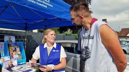 Eine Beamtin der Polizei steht am Infostand für Kriminalprävention und unterhält sich mit einem Mann.