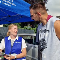 Eine Beamtin der Polizei steht am Infostand für Kriminalprävention und unterhält sich mit einem Mann.