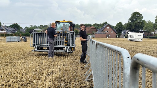 Zwei junge Männer stellen Zäune auf einem Feld auf.