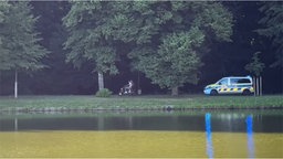 Zwei Menschen sitzen auf einem Motorroller und fliehen vor einem Polizeiwagen.