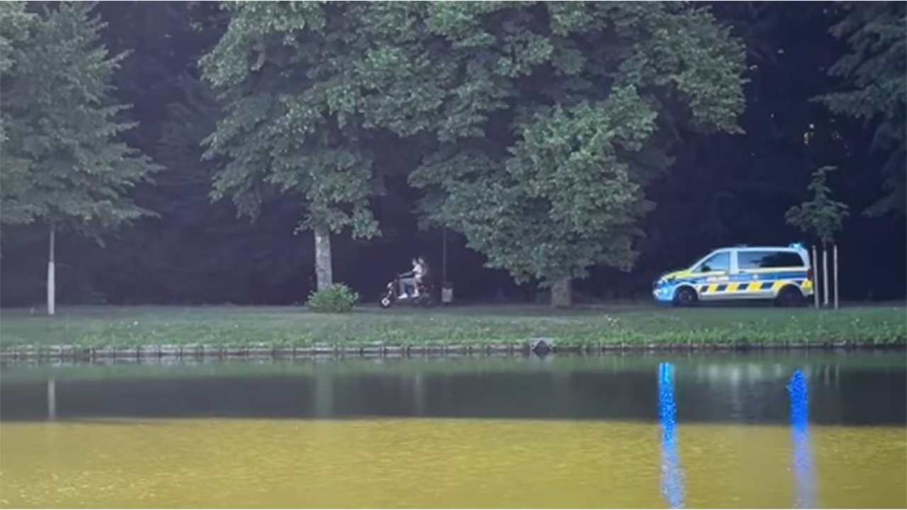 Zwei Menschen sitzen auf einem Motorroller und fliehen vor einem Polizeiwagen.