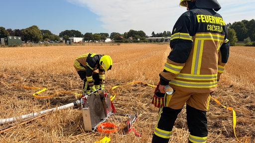 Mehrere Feuerwehrleute packen einen Löschschlauch aus einem Metallkoffer aus.